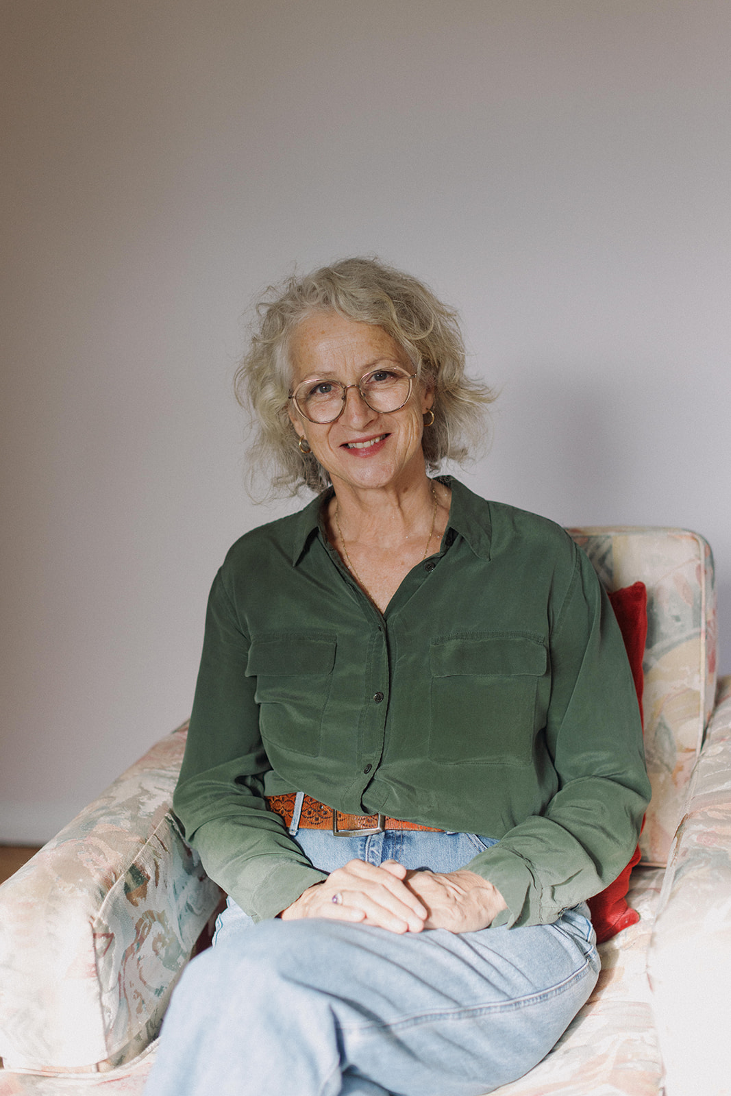 Sue Lansdown seated on a softly patterned vintage couch, smiling warmly at the camera.